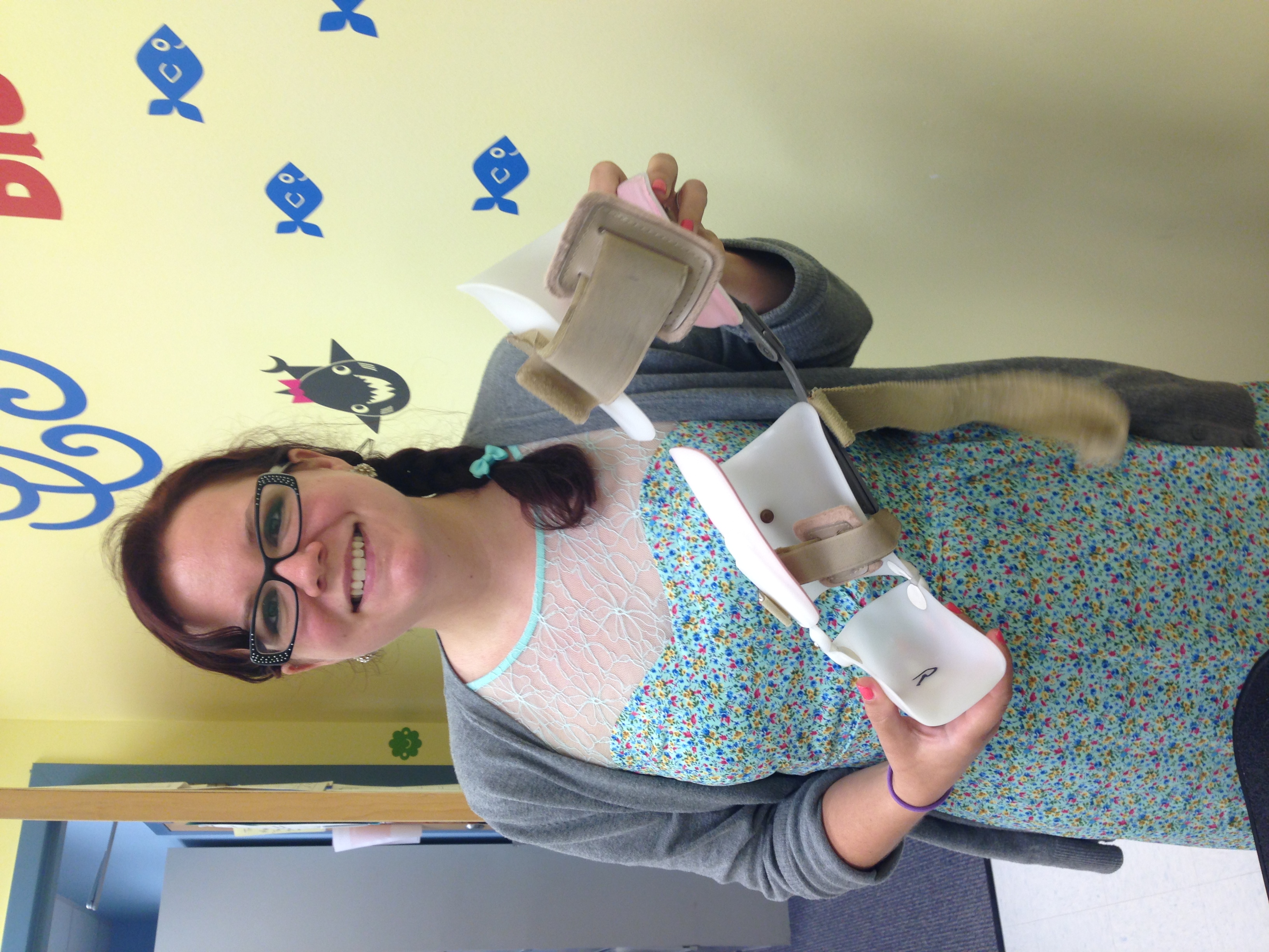 Rebeca in her baby shark themed patient treatment room, holding an AFO